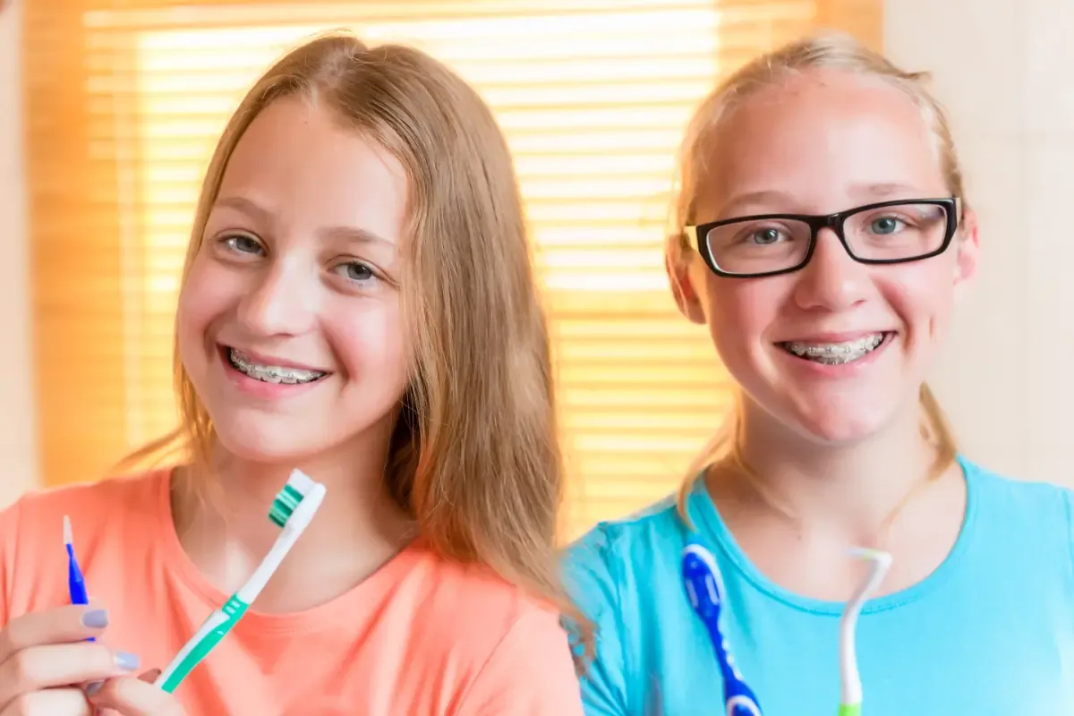 Two girls with braces holding toothbrushes